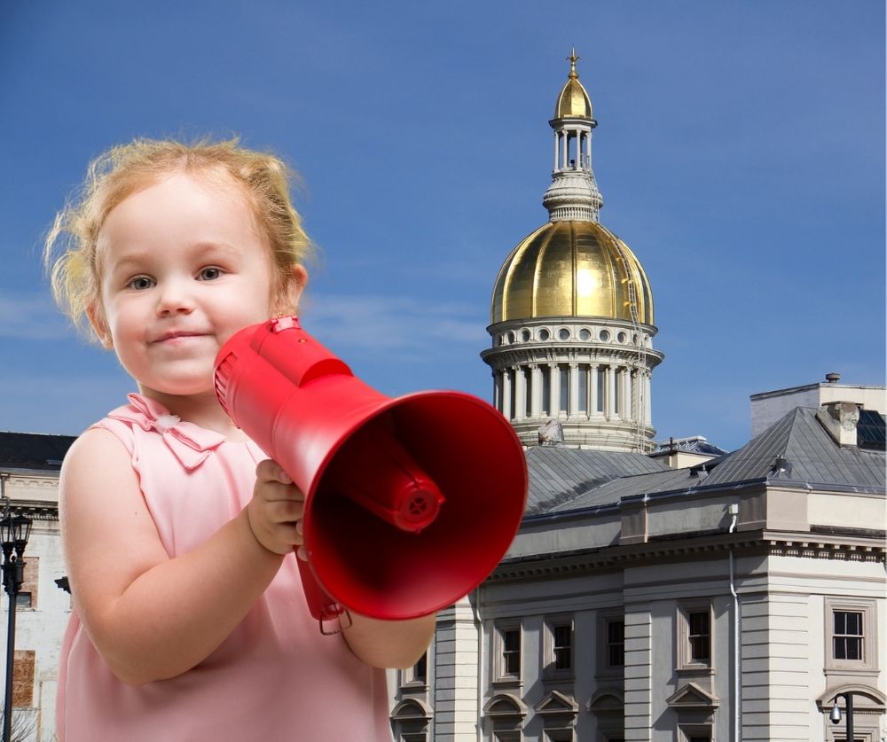 Blonde toddler with megaphone in front of statehouse