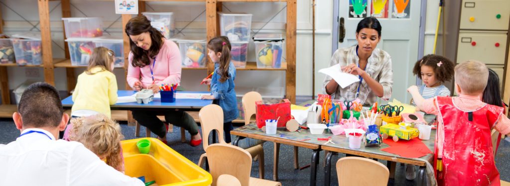 Class of nursery children doing arts and crafts with their teachers. They are using recycled boxes and cartons.